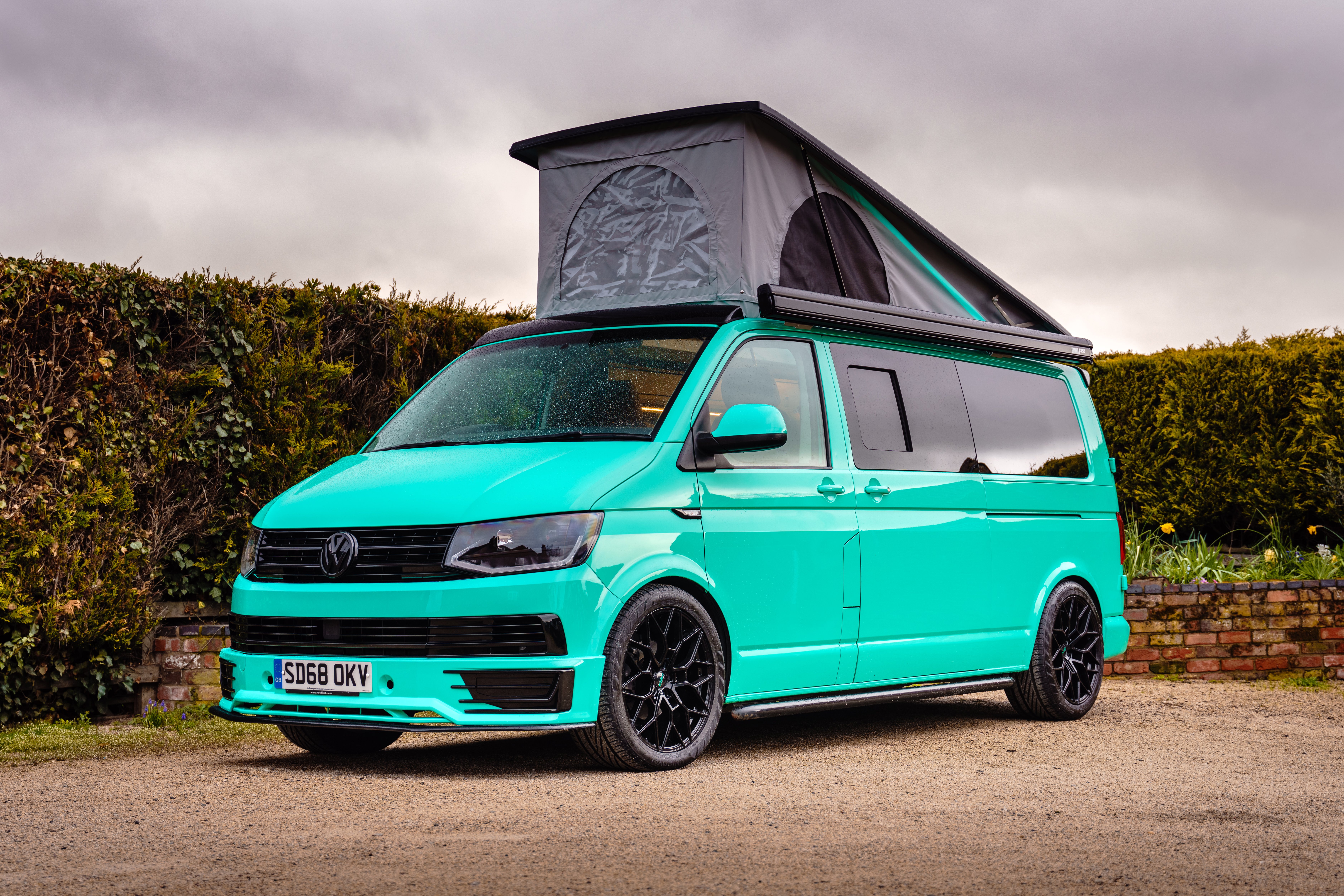 A turquoise campervan parked outdoors with its pop-top roof extended, demonstrating the design, build quality, and added height benefits to consider before investing in a pop-top roof for your van.